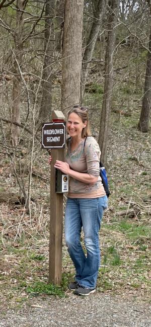 photo of Kathryn Newfont smiling next to a trail marker in woods