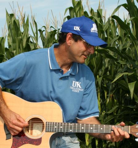 photo of Paul Vincelli playing guitart in a field of tall plants