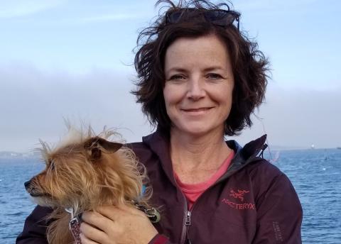 headshot of Rhonda Davis holding a dog in front of an ocean