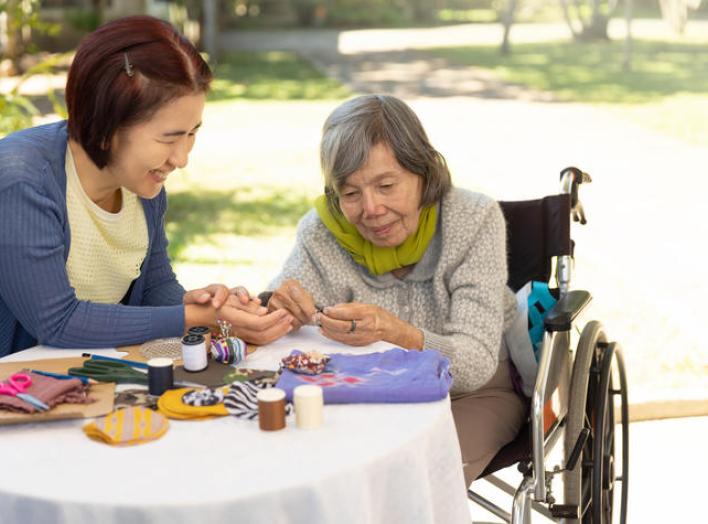 Young woman sitting with old woman in wheelchair doing drafts