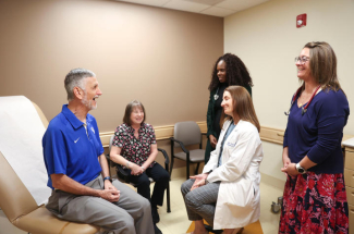 Gerald Klim sits in a medical evaluation room and laughs with his wife and care team